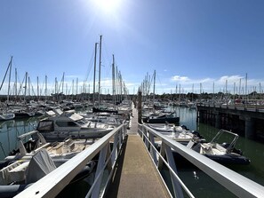 Ein Yachthafen mit vertäuten Booten, einer Holzpromenade und blauem Himmel.