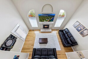 Ein Wohnzimmer mit Kamin, Dartscheibe, einem schwarzen Ledersofa und einem Fernseher, der eine schöne Aussicht zeigt.
