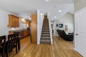 Eine Küche mit Holzausstattung, ein Essbereich mit Stühlen, eine Treppe und ein Wohnzimmer mit einer Couch.