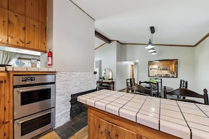 A kitchen with wooden cabinets, a tiled countertop, a built-in oven, and a dining area with a table and chairs.