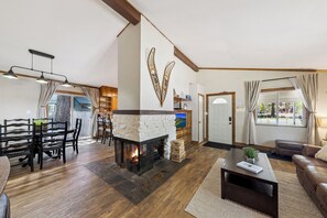 A living room with a stone fireplace, wooden furniture, a television, and a view through a large window.