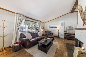 A living room with a brown leather sofa, a coffee table, a fireplace, and a large window with curtains.