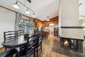 A modern kitchen with wooden cabinets, a stone fireplace, and a dining area with a round table and chairs.