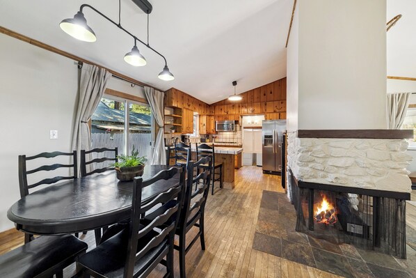 A modern kitchen with wooden cabinets, a stone fireplace, and a dining area with a round table and chairs.