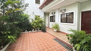 Un patio con plantas en macetas, suelo de baldosas y un edificio con unidades de aire acondicionado.