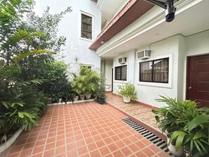 Pátio com plantas em vasos, piso de azulejos e um edifício com aparelhos de ar condicionado.