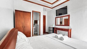 Habitación de hotel con cama, armario de madera, escritorio con espejo, televisión y baño visible a través de una puerta abierta.