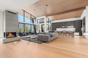 A spacious living area with a fireplace, a grey sofa, and a dining area with bar stools. - The Mountaintop at Kadenwood | Ski in Ski out (Whistler)