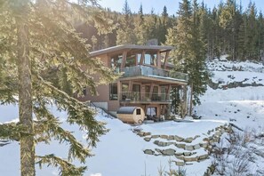A multi-level wooden cabin with a balcony, surrounded by snow and trees. - The Mountaintop | Kadenwood Ski In Ski Out | Views (Whistler)
