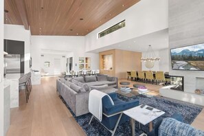 A spacious living area with a large sectional sofa, a dining area with yellow chairs, and a kitchen with a modern refrigerator. - The Mountaintop | Kadenwood Ski In Ski Out | Views (Whistler)