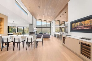 A modern kitchen with large windows, a dining area with chairs, and a sofa. - The Mountaintop at Kadenwood | Ski in Ski out (Whistler)