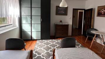 Quarto com cama, duas cadeiras, cômoda, janela com cortinas e um quadro na parede.