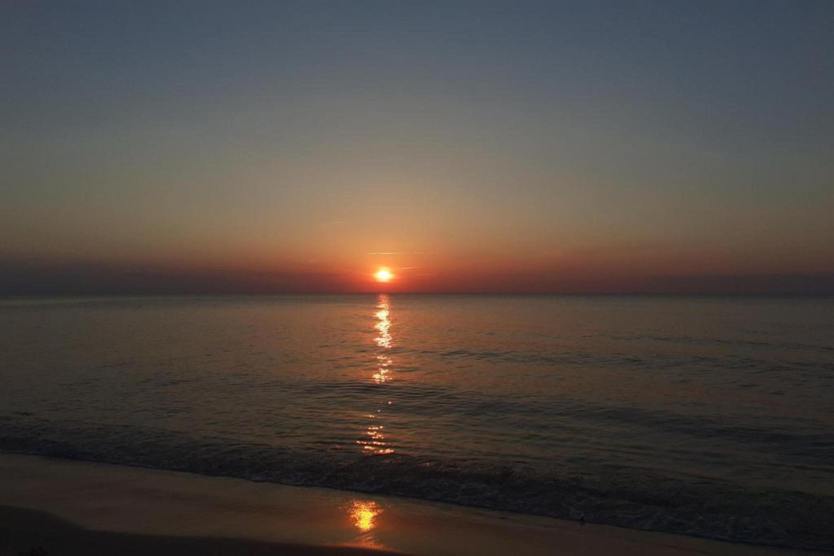 A sunset over a calm sea with gentle waves.