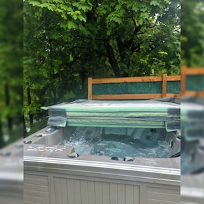 A hot tub with a wooden deck and a metal railing, surrounded by trees.