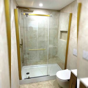 A glass-enclosed shower with a white toilet and a wooden cabinet. - Tropical Refuge (Chambly)