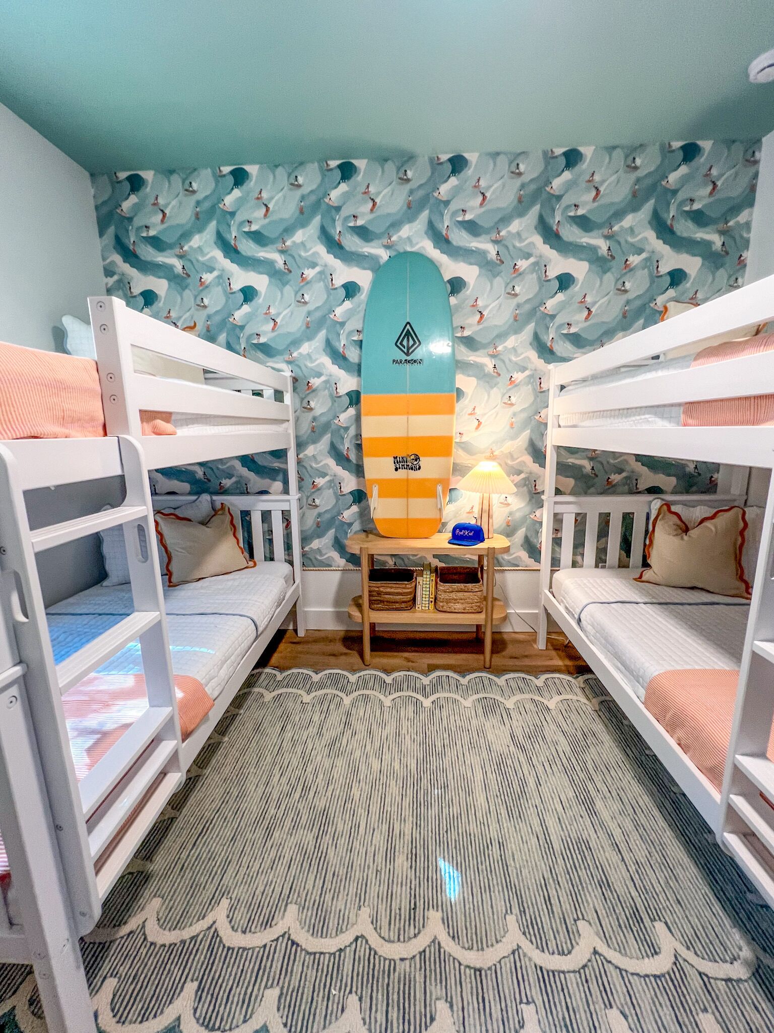 A room with bunk beds, a surfboard, a lamp, and a patterned wall.