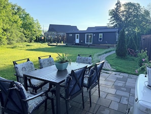 A patio with a table and chairs, a lawn, and a house in the background. - Garden Resort of Niagara Retreat Center  (Niagara Falls)