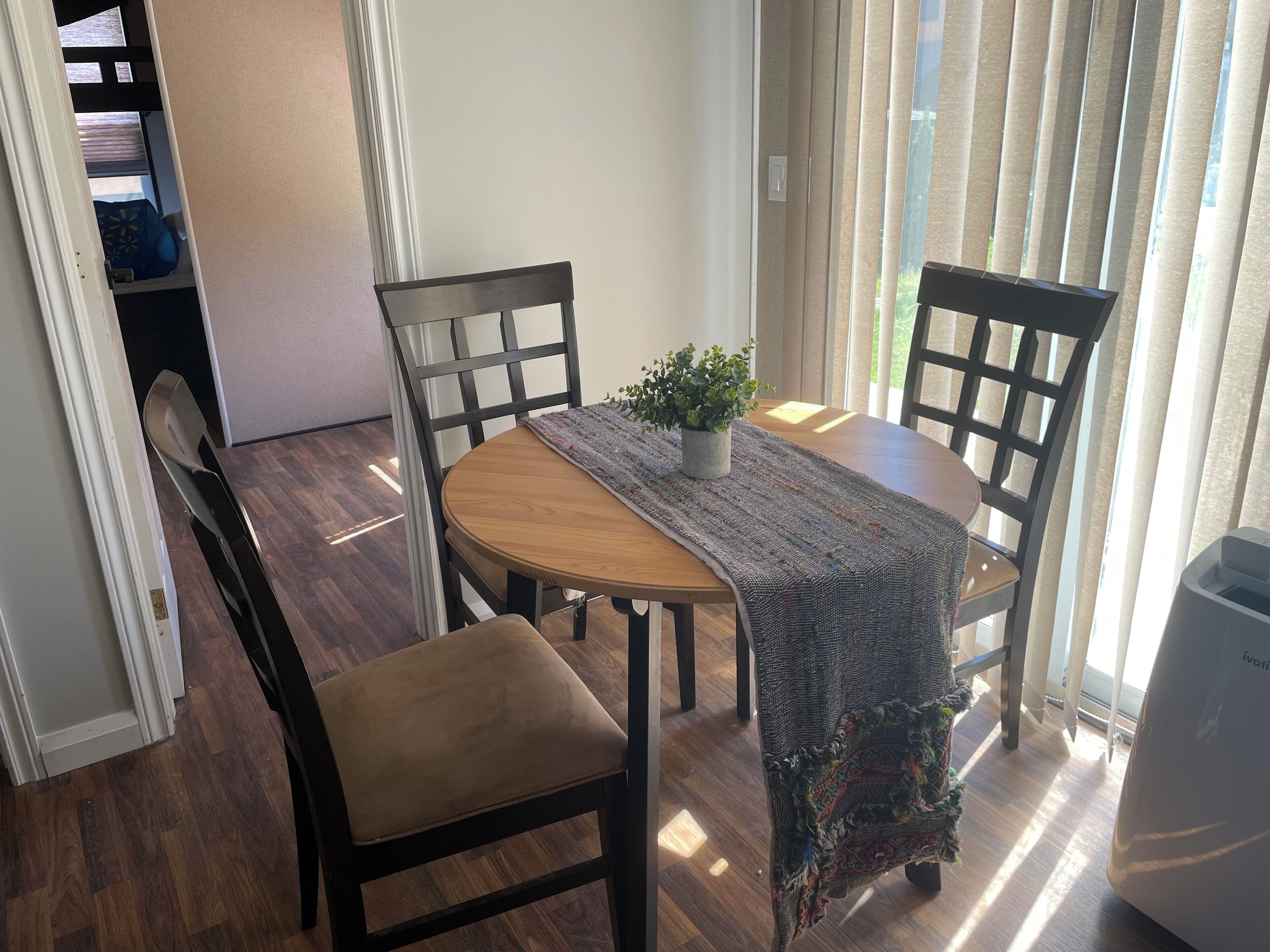 Un comedor con una mesa de madera redonda, dos sillas, una planta en maceta y un mantel decorado.