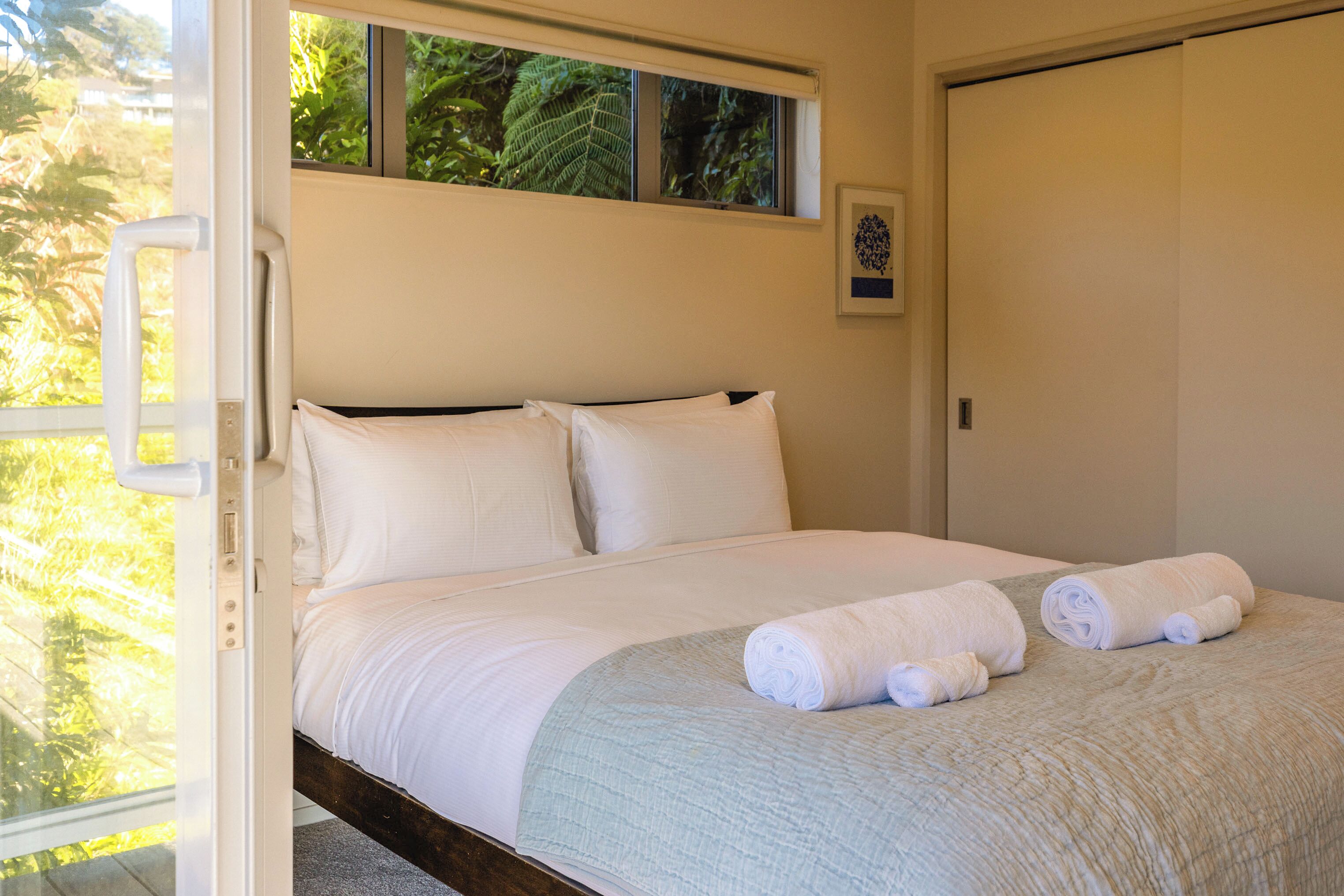 A bed with white linens, a light blue quilt, and rolled towels.