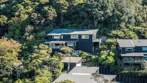 A modern two-story house surrounded by dense forest. - Miro Ridge in Palm Beach (Waiheke Island)
