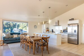 A modern kitchen with a central island, wooden chairs, a dining table, and a large window with a view of trees.