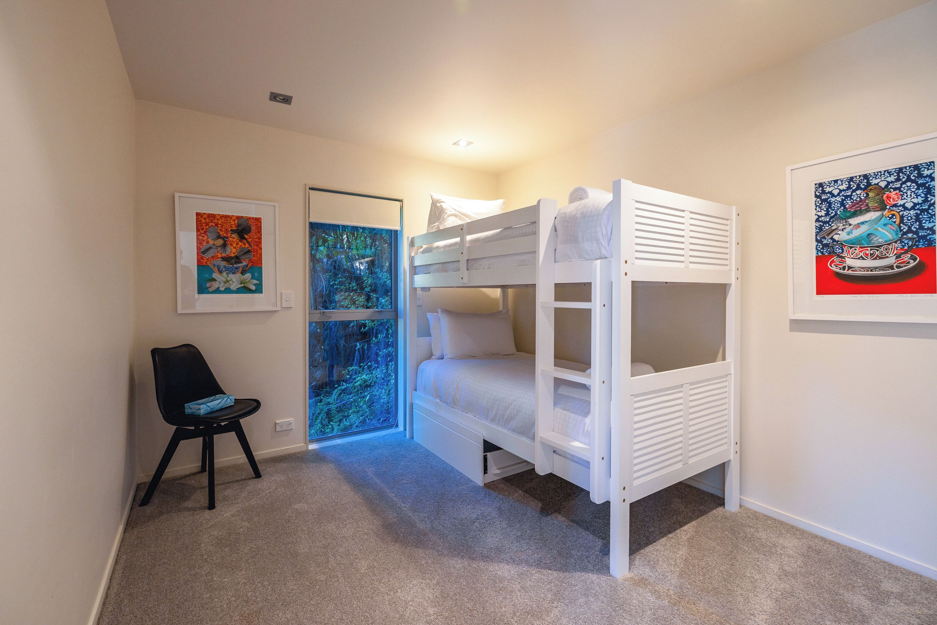 Quarto com beliche, uma cadeira, duas obras de arte emolduradas e uma porta que dá para outro quarto.
