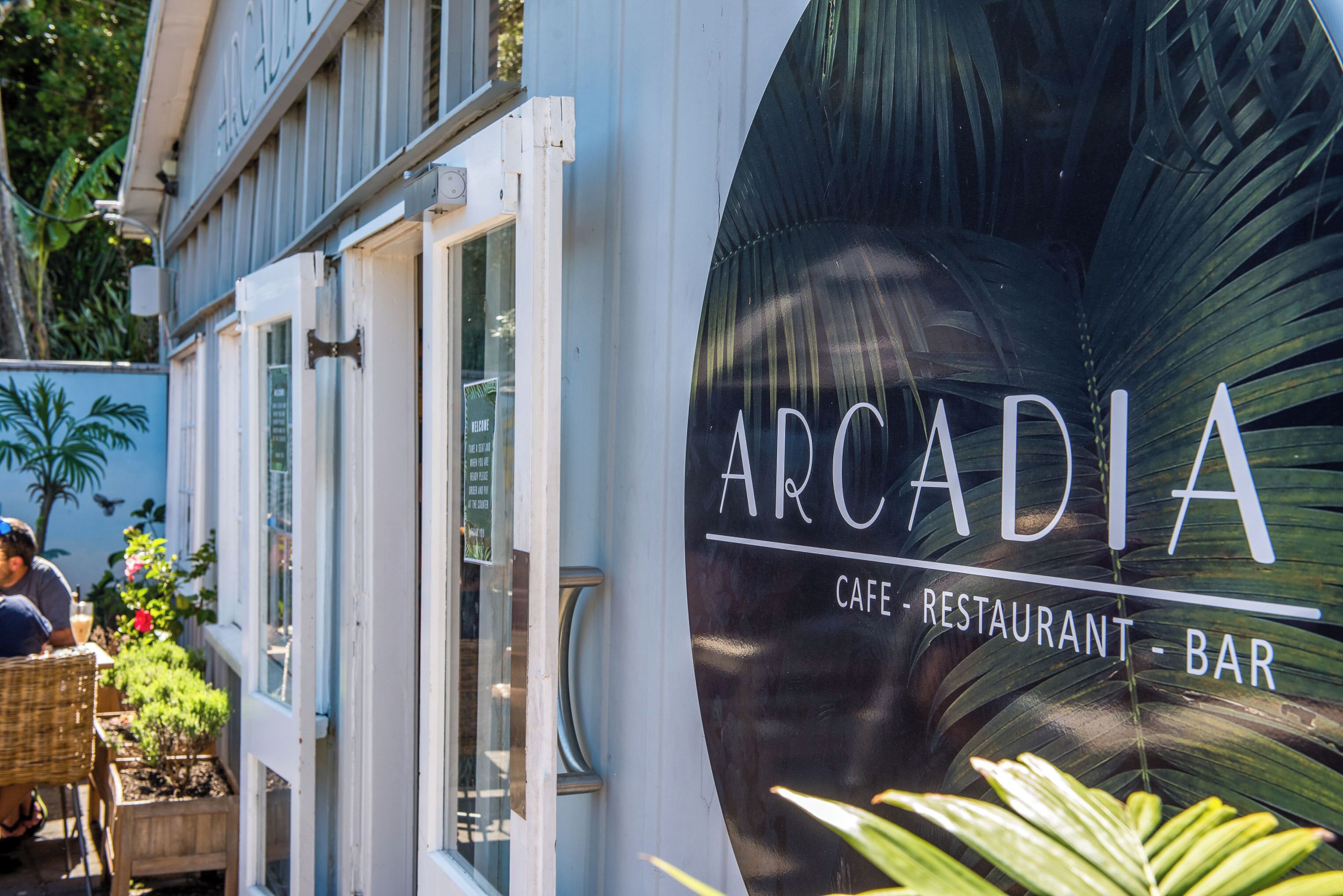 A cafe with a large sign reading 'ARCADIA' and a visible outdoor seating area with wicker furniture.