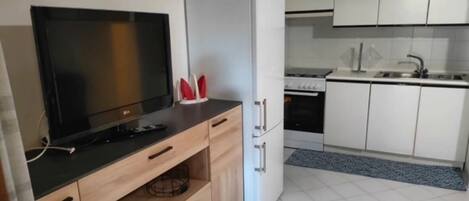A modern kitchen with a flat-screen TV, a white refrigerator, and white cabinets.