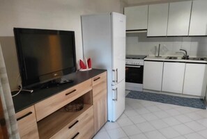 A modern kitchen with a flat-screen TV, a white refrigerator, and white cabinets.
