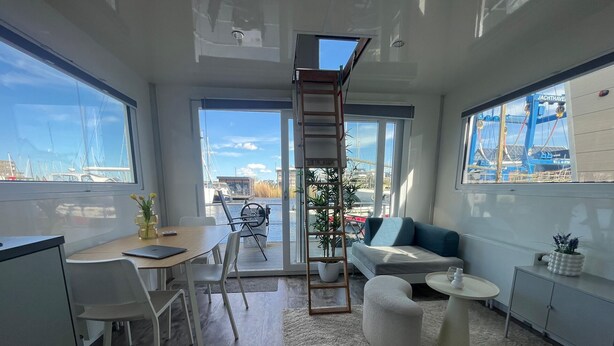 Un interior moderno con escritorio, zona de estar y ventanas amplias con vistas a un puerto deportivo.
