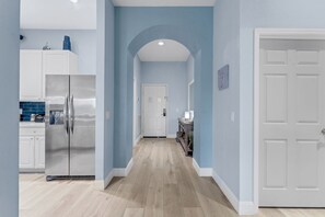 Eine Küche mit weißen Schränken, einem Edelstahlkühlschrank und einer blauen Fliesenwand.