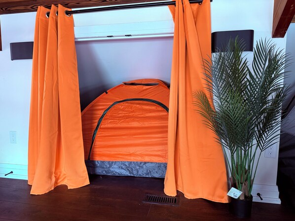 Eine zeltähnliche Struktur mit orangefarbenem Stoff, einem Blumentopf und einem Holzboden.