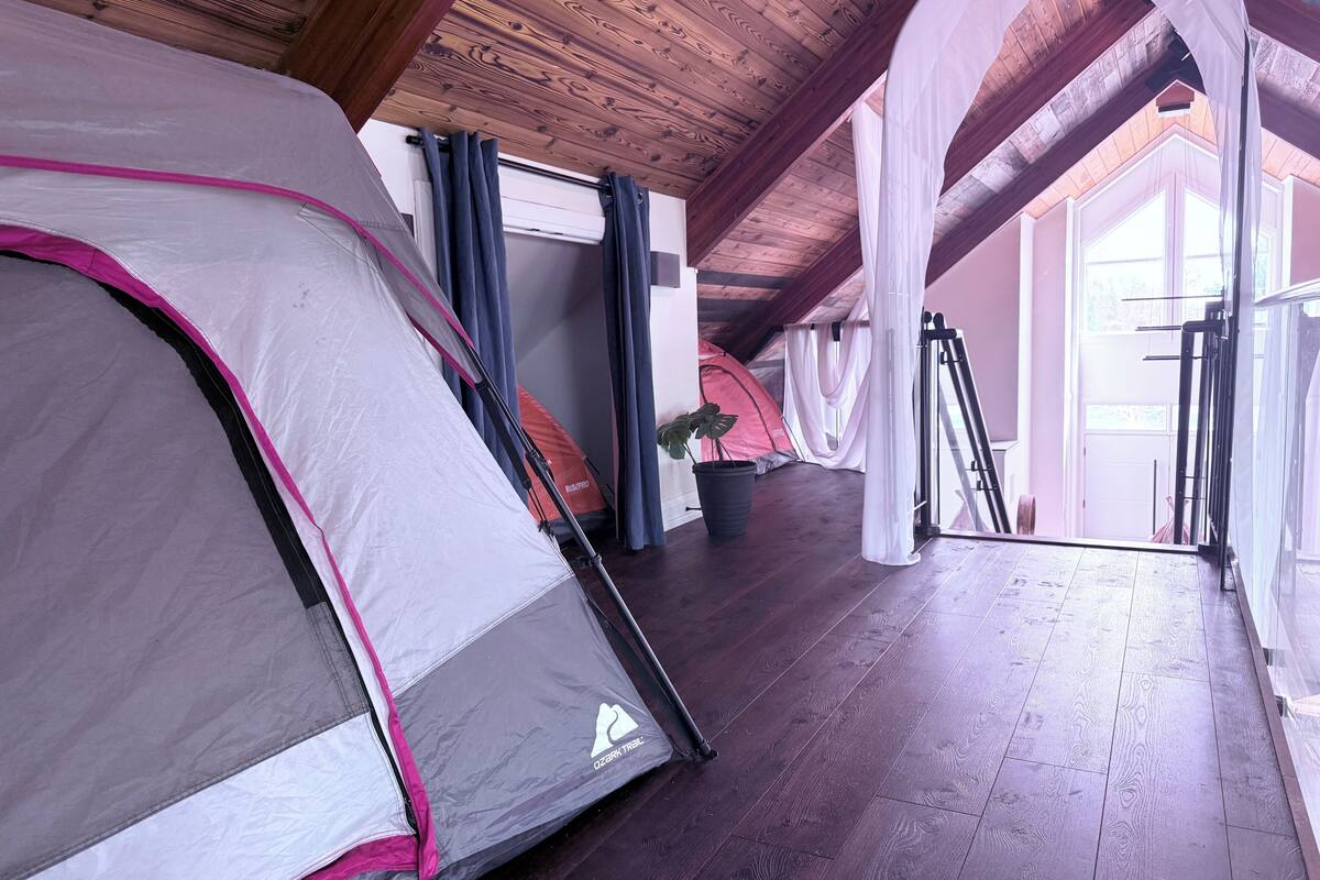 Una habitación con techo alto, vigas de madera y varias tiendas de campaña montadas.