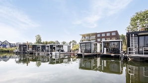Une propriété située au bord d’un canal, avec des bâtiments modernes, un bateau amarré et un ciel dégagé.