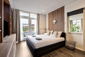 Une chambre à coucher moderne avec un grand lit, une télévision, un plancher en bois et une vue sur l’extérieur.