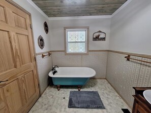 Une salle de bain avec une baignoire sur pieds, une porte en bois et une fenêtre avec des stores.