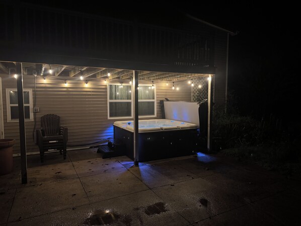 Un espacio exterior techado con jacuzzi, asientos e iluminación colgante.