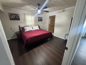 A bedroom with a bed, a ceiling fan, a door, and a window with curtains.