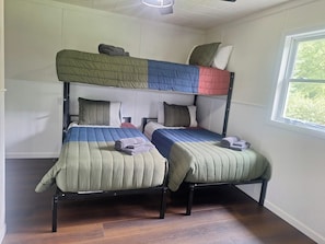 A room with two bunk beds, a window with a view of trees, and a ceiling fan.