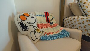 A chair with a Snoopy-themed pillow and a blanket with a checkered pattern.