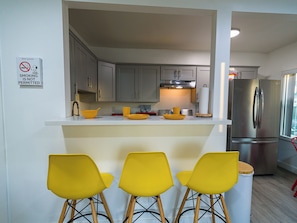 A modern kitchen with a bar area, a stainless steel refrigerator, and a no-smoking sign.