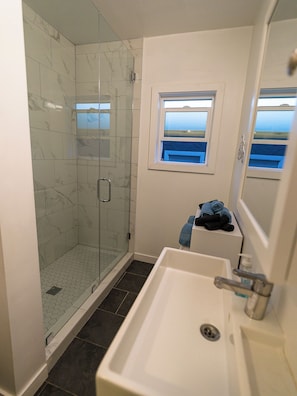 A bathroom with a glass shower enclosure, a sink, and a window with a view.