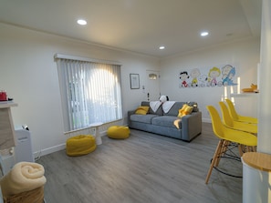 A modern living room with a grey sofa, yellow bean bag chairs, and a dining area with yellow chairs.