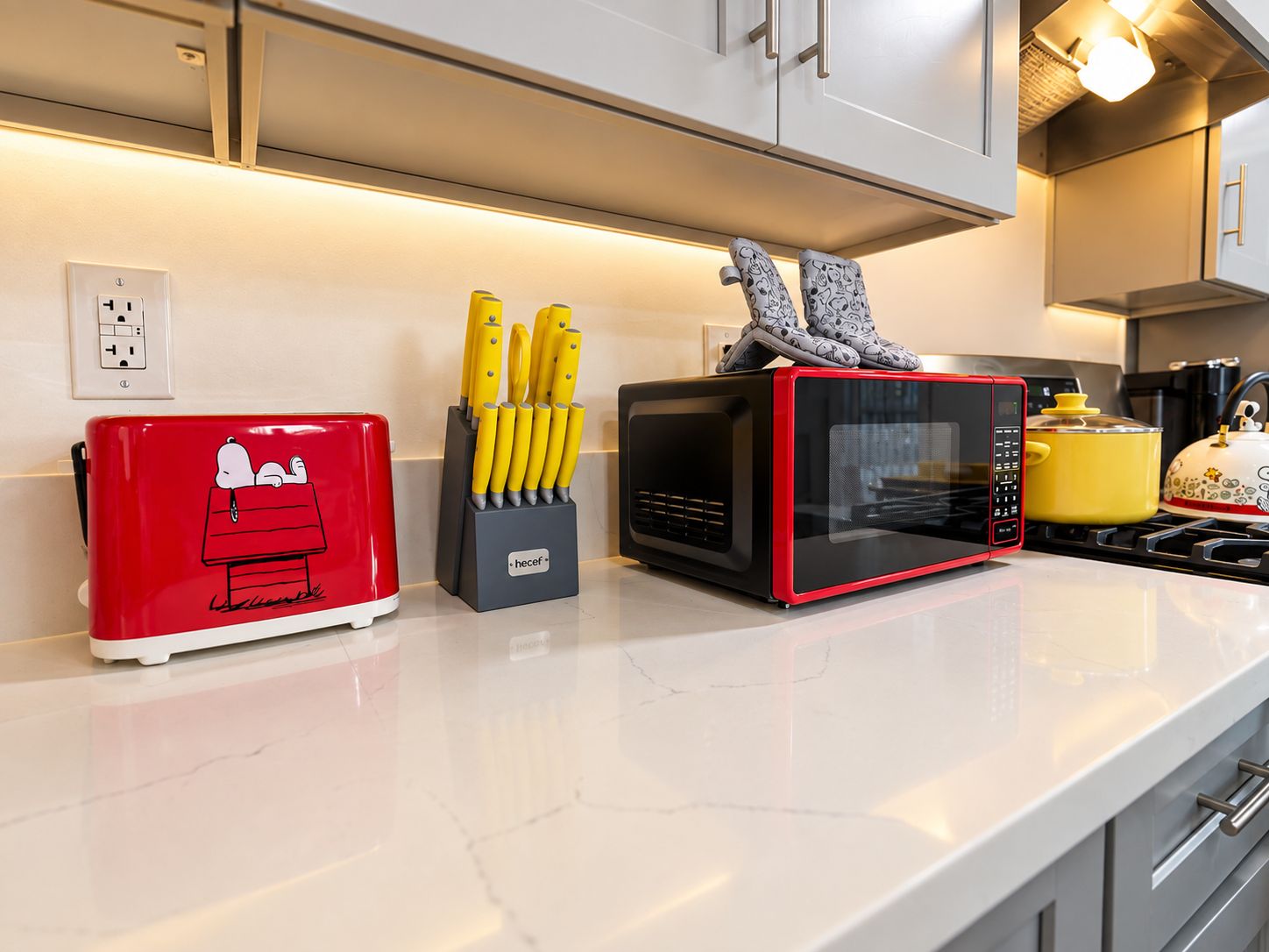 A kitchen with a red toaster, a black microwave, and a knife block with yellow handles.