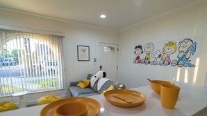 A modern living room with a sofa, a wall with cartoon characters, and a window with blinds.