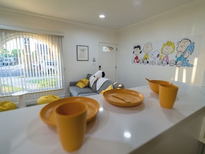 A modern living room with a sofa, a wall with cartoon characters, and a window with blinds.
