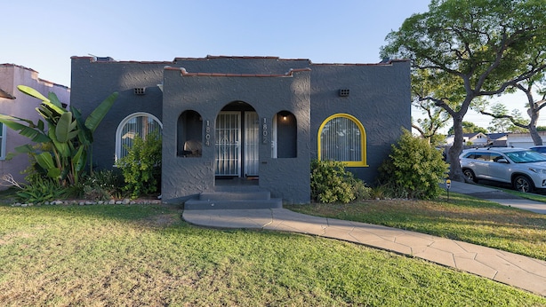 A two-story house with a stucco exterior, arched windows, and a front yard with a sidewalk.