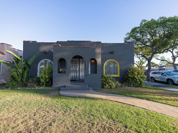 A two-story house with a stucco exterior, arched windows, and a front yard with a sidewalk.