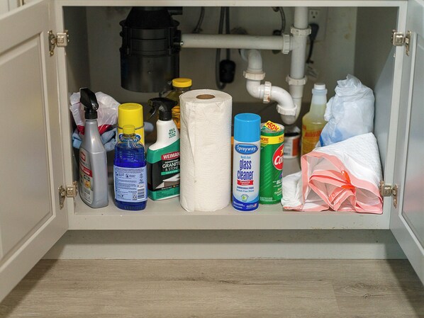 Um armário com produtos de limpeza, um rolo de papel toalha e um saco plástico.