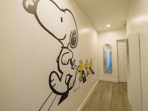 A hallway with a wall mural of Snoopy and a mirror reflecting the room.